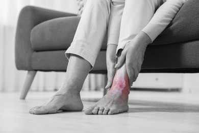 Image of Arthritis. Woman suffering from pain in leg at home, closeup. Black and white toning with red color accent