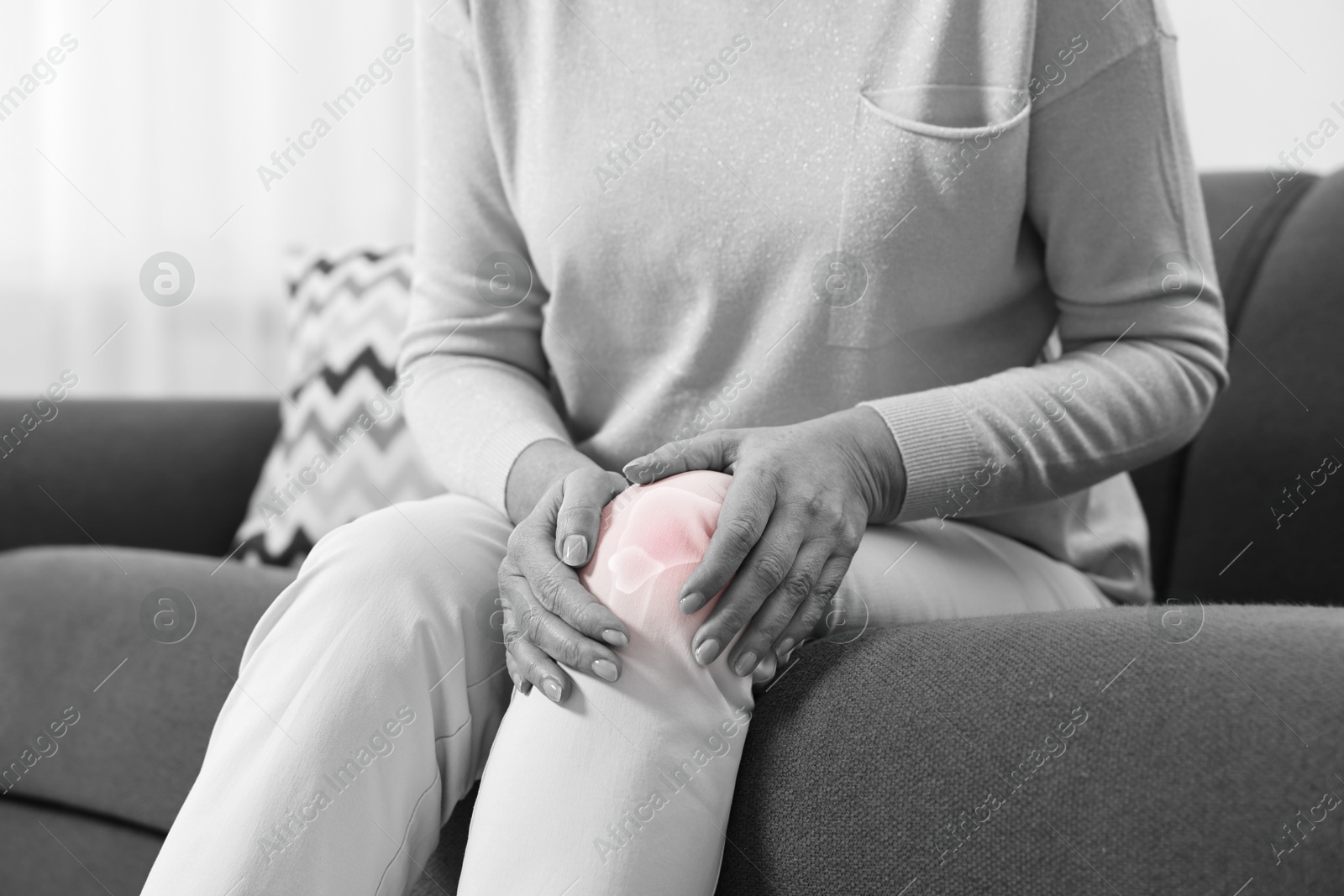 Senior woman suffering from pain in knee on sofa at home, closeup. Black and white toning with red color accent Image of Senior woman suffering from pain in knee on sofa at home, closeup. Black and white toning with red color accent