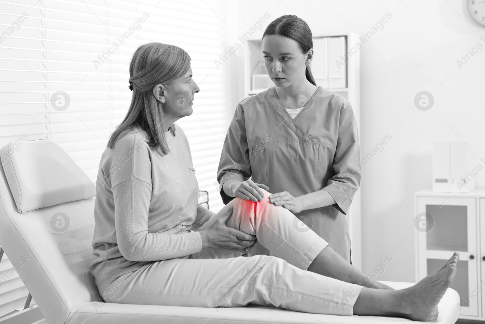 Arthritis. Doctor examining patient with knee pain in hospital. Black and white toning with red color accent Image of Arthritis. Doctor examining patient with knee pain in hospital. Black and white toning with red color accent