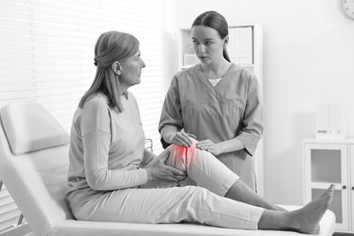 Image of Arthritis. Doctor examining patient with knee pain in hospital. Black and white toning with red color accent