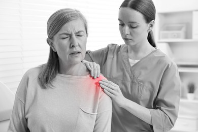 Image of Arthritis. Doctor examining patient with shoulder pain in hospital. Black and white toning with red color accent
