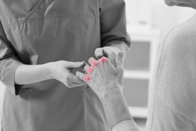 Image of Arthritis. Doctor examining patient's hand in hospital, closeup. Black and white toning with red color accent