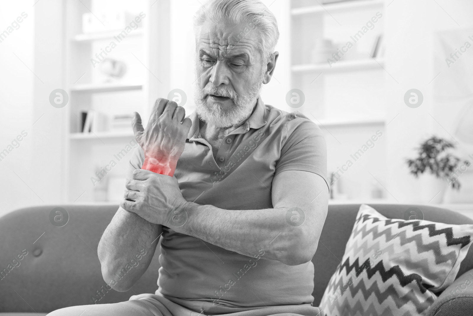 Image of Arthritis. Senior man suffering from wrist pain on sofa at home. Black and white toning with red color accent