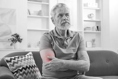 Image of Arthritis. Senior man suffering from pain in elbow at home. Black and white toning with red color accent