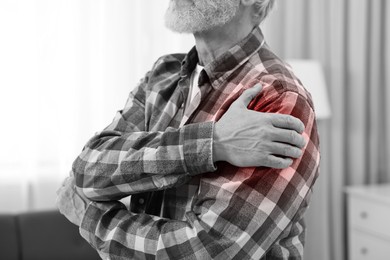 Image of Arthritis. Senior man suffering from pain in shoulder at home, closeup. Black and white toning with red color accent