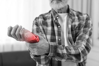 Image of Arthritis. Senior man suffering from wrist pain indoors, closeup. Black and white toning with red color accent