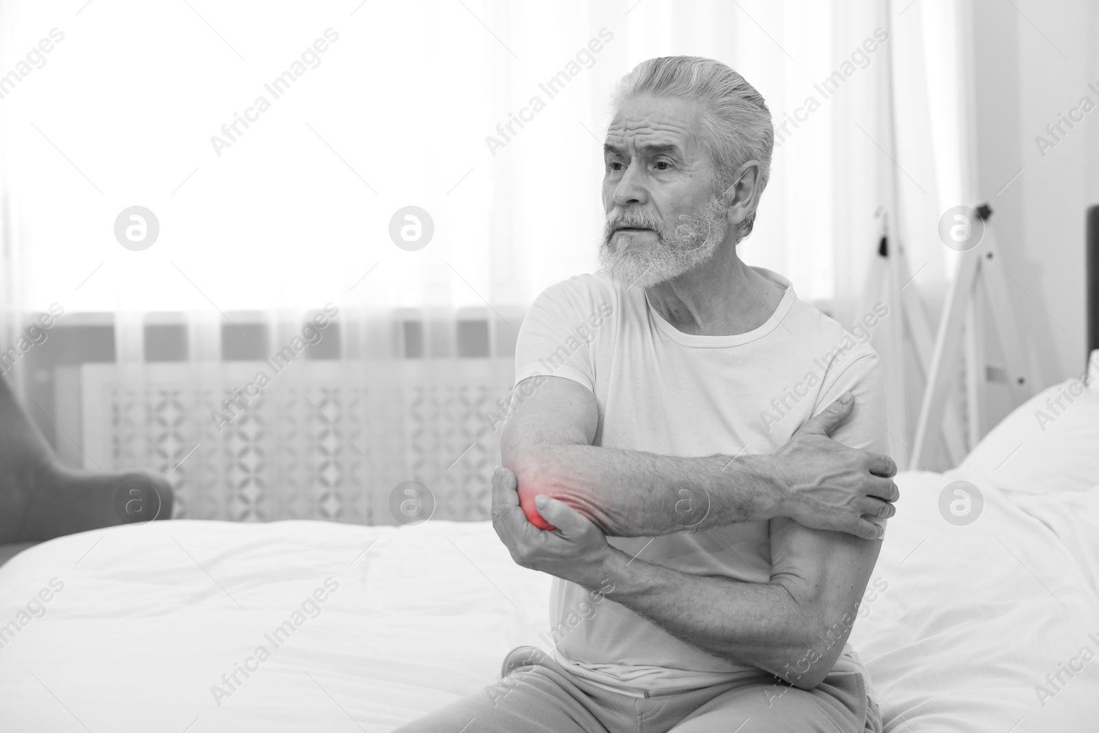 Arthritis. Senior man suffering from pain in elbow at home. Black and white toning with red color accent Image of Arthritis. Senior man suffering from pain in elbow at home. Black and white toning with red color accent