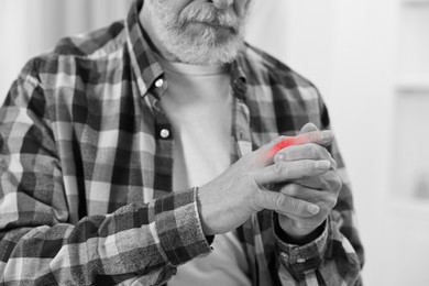 Image of Arthritis. Senior man suffering from pain in finger indoors, closeup. Black and white toning with red color accent