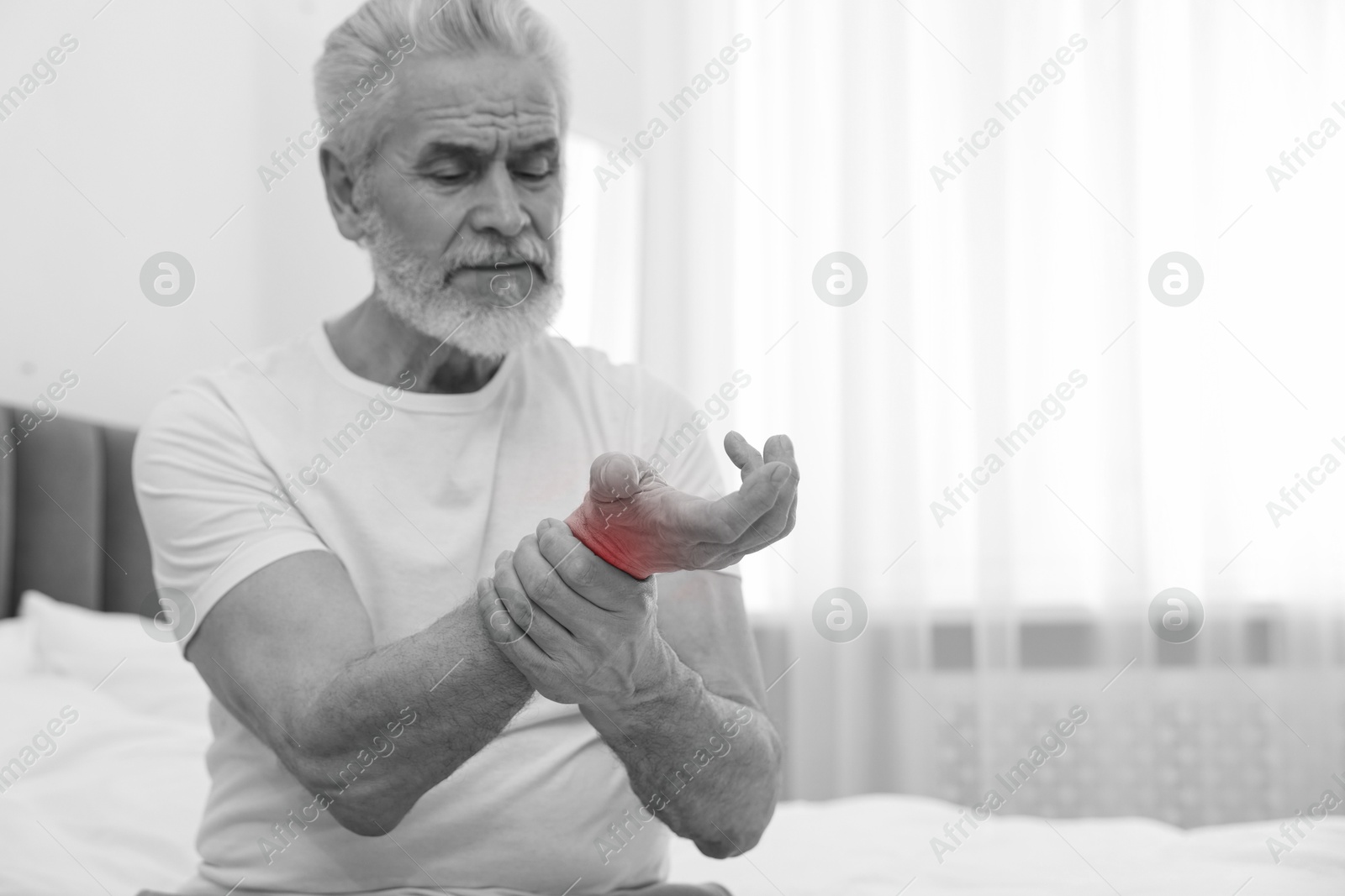 Arthritis. Senior man suffering from wrist pain on bed at home. Black and white toning with red color accent Image of Arthritis. Senior man suffering from wrist pain on bed at home. Black and white toning with red color accent