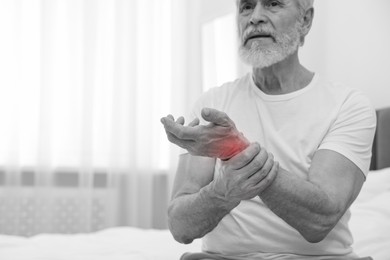 Image of Arthritis. Senior man suffering from wrist pain on bed at home. Black and white toning with red color accent