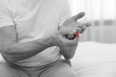 Image of Arthritis. Man suffering from pain in finger on bed at home, closeup. Black and white toning with red color accent