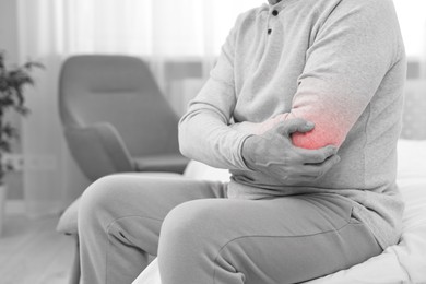 Image of Arthritis. Man suffering from pain in elbow at home, closeup. Black and white toning with red color accent