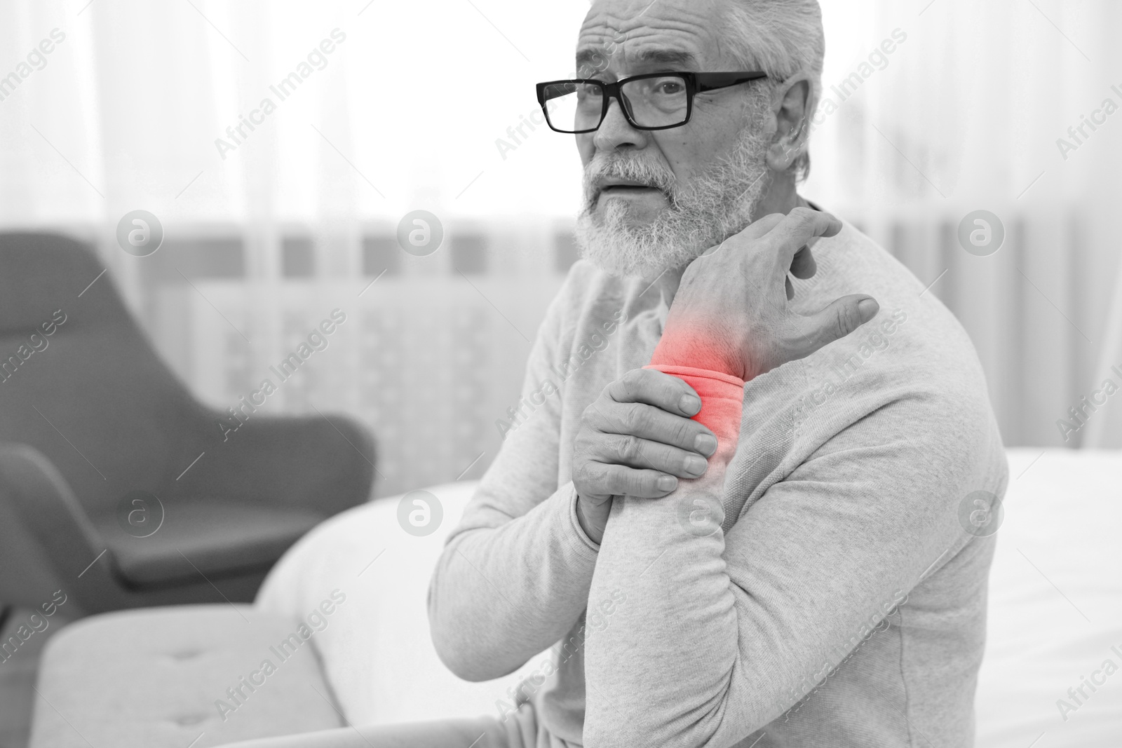 Arthritis. Senior man suffering from wrist pain at home. Black and white toning with red color accent Image of Arthritis. Senior man suffering from wrist pain at home. Black and white toning with red color accent