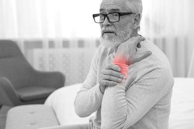 Image of Arthritis. Senior man suffering from wrist pain at home. Black and white toning with red color accent