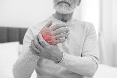 Image of Arthritis. Senior man suffering from pain in hand at home, closeup. Black and white toning with red color accent