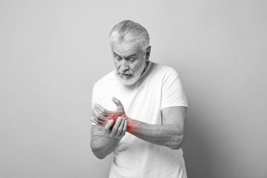 Image of Arthritis. Senior man suffering from pain in wrist. Black and white toning with red color accent