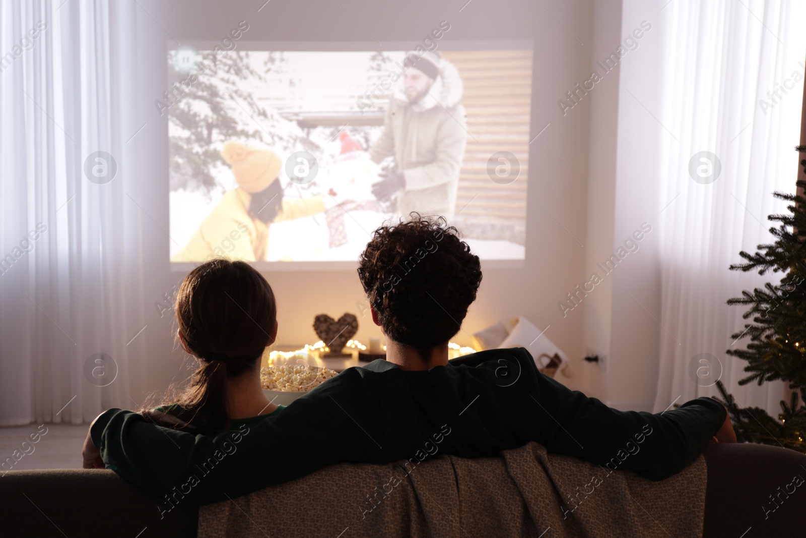 Couple watching romantic Christmas movie via video projector at home, back view Photo of Couple watching romantic Christmas movie via video projector at home, back view