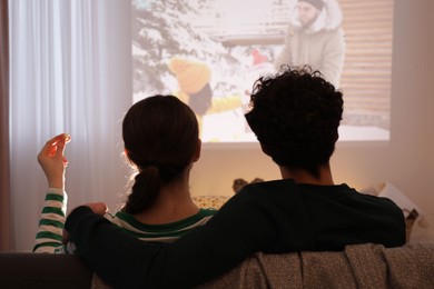 Photo of Couple watching romantic Christmas movie via video projector at home, back view