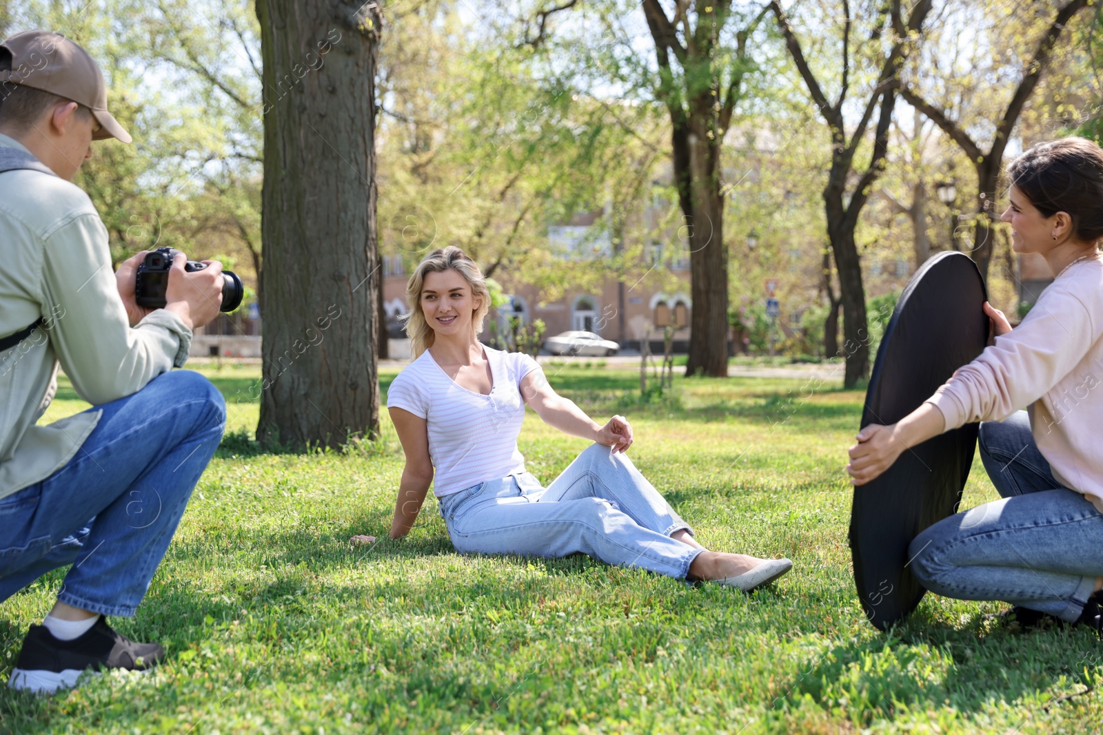Professional photographers with reflector and camera near model during shooting outdoors on sunny day Photo of Professional photographers with reflector and camera near model during shooting outdoors on sunny day