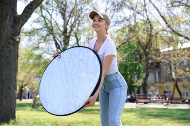 Photo of Woman with reflector outdoors on sunny day. Photography equipment
