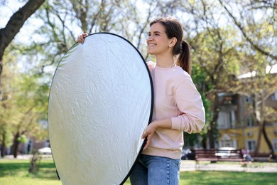 Photo of Woman with reflector outdoors on sunny day. Photography equipment