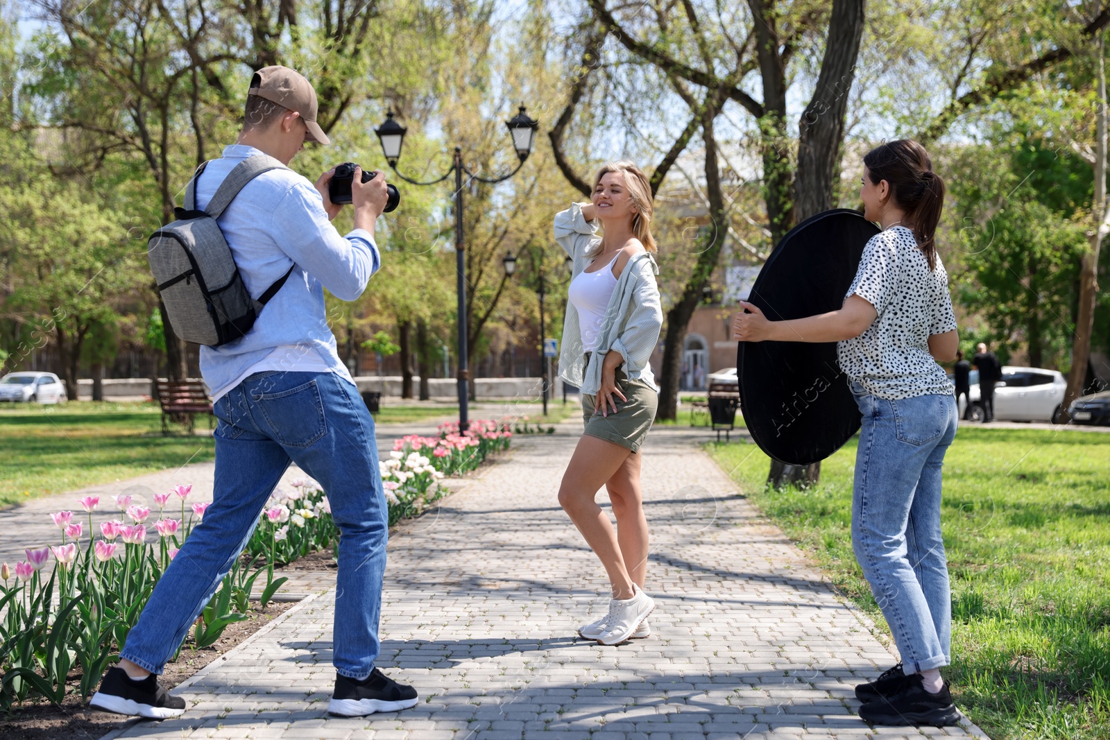 Professional photographers with reflector and camera near model during shooting outdoors on sunny day Photo of Professional photographers with reflector and camera near model during shooting outdoors on sunny day