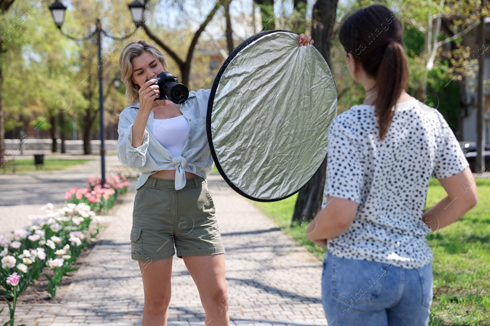 Professional photographer with reflector and camera near model during shooting outdoors on sunny day Photo of Professional photographer with reflector and camera near model during shooting outdoors on sunny day