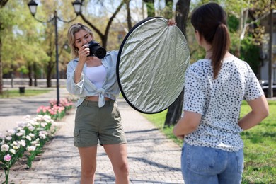 Photo of Professional photographer with reflector and camera near model during shooting outdoors on sunny day