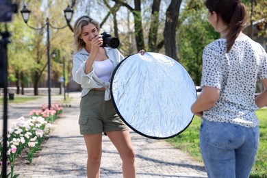 Photo of Professional photographer with reflector and camera near model during shooting outdoors on sunny day