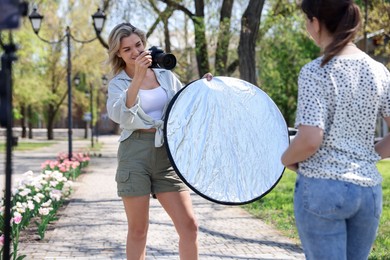Photo of Professional photographer with reflector and camera near model during shooting outdoors on sunny day