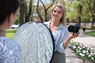 Photo of Professional photographer with reflector and camera near model during shooting outdoors on sunny day
