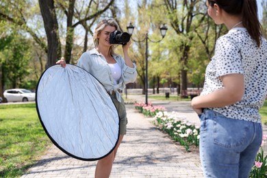 Photo of Professional photographer with reflector and camera near model during shooting outdoors on sunny day