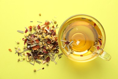 Photo of Delicious herbal tea in glass cup and dry leaves on green background, flat lay