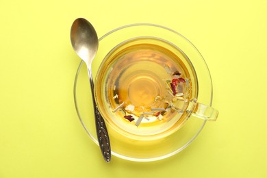 Photo of Delicious herbal tea in glass cup and spoon on green background, top view