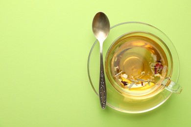 Photo of Delicious herbal tea in glass cup and spoon on light green background, top view. Space for text