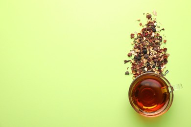 Photo of Delicious herbal tea in glass cup and dry leaves on light green background, flat lay. Space for text