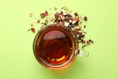 Photo of Delicious herbal tea in glass cup and dry leaves on light green background, flat lay