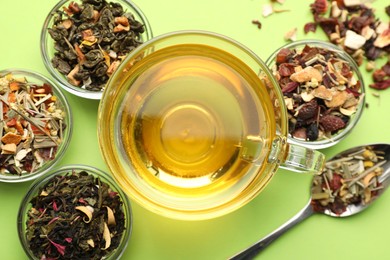 Photo of Delicious herbal tea in glass cup and dry leaves on light green background, flat lay