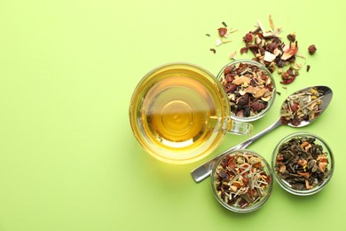 Photo of Delicious herbal tea in glass cup and dry leaves on light green background, flat lay. Space for text