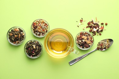 Photo of Delicious herbal tea in glass cup and dry leaves on light green background, flat lay