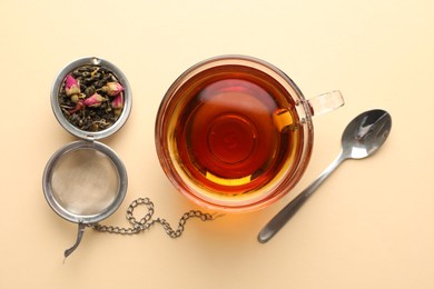 Photo of Delicious herbal tea in glass cup, dry leaves and spoon on beige background, flat lay