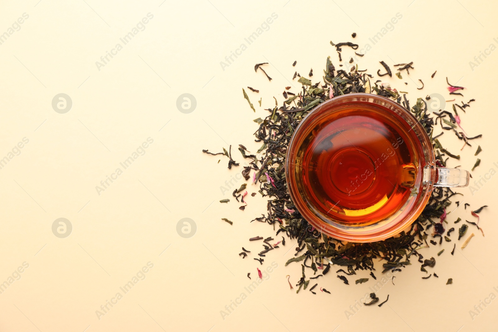 Delicious herbal tea in glass cup and dry leaves on beige background, flat lay. Space for text Photo of Delicious herbal tea in glass cup and dry leaves on beige background, flat lay. Space for text