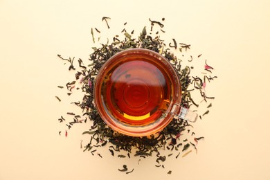 Photo of Delicious herbal tea in glass cup and dry leaves on beige background, flat lay