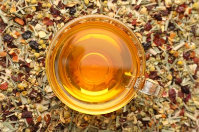Photo of Delicious herbal tea in glass cup on dry leaves, top view