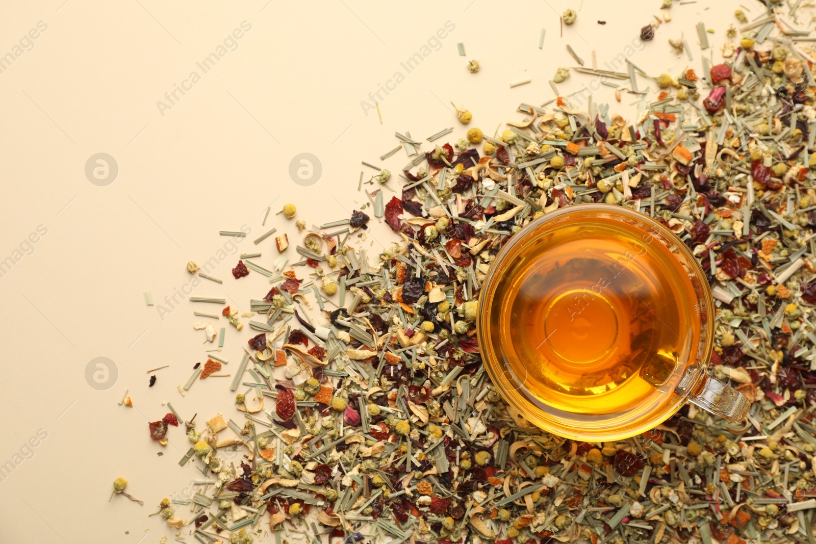 Delicious herbal tea in glass cup and dry leaves on beige background, top view. Space for text Photo of Delicious herbal tea in glass cup and dry leaves on beige background, top view. Space for text
