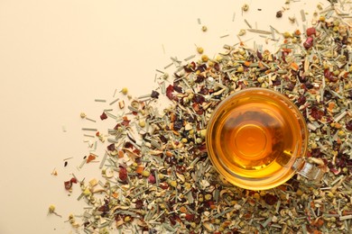 Photo of Delicious herbal tea in glass cup and dry leaves on beige background, top view. Space for text
