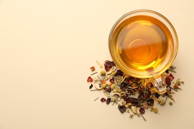 Photo of Delicious herbal tea in glass cup and dry leaves on beige background, flat lay. Space for text