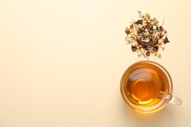 Photo of Delicious herbal tea in glass cup and dry leaves on beige background, flat lay. Space for text