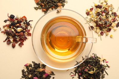 Photo of Delicious herbal tea in glass cup and dry leaves on beige background, flat lay