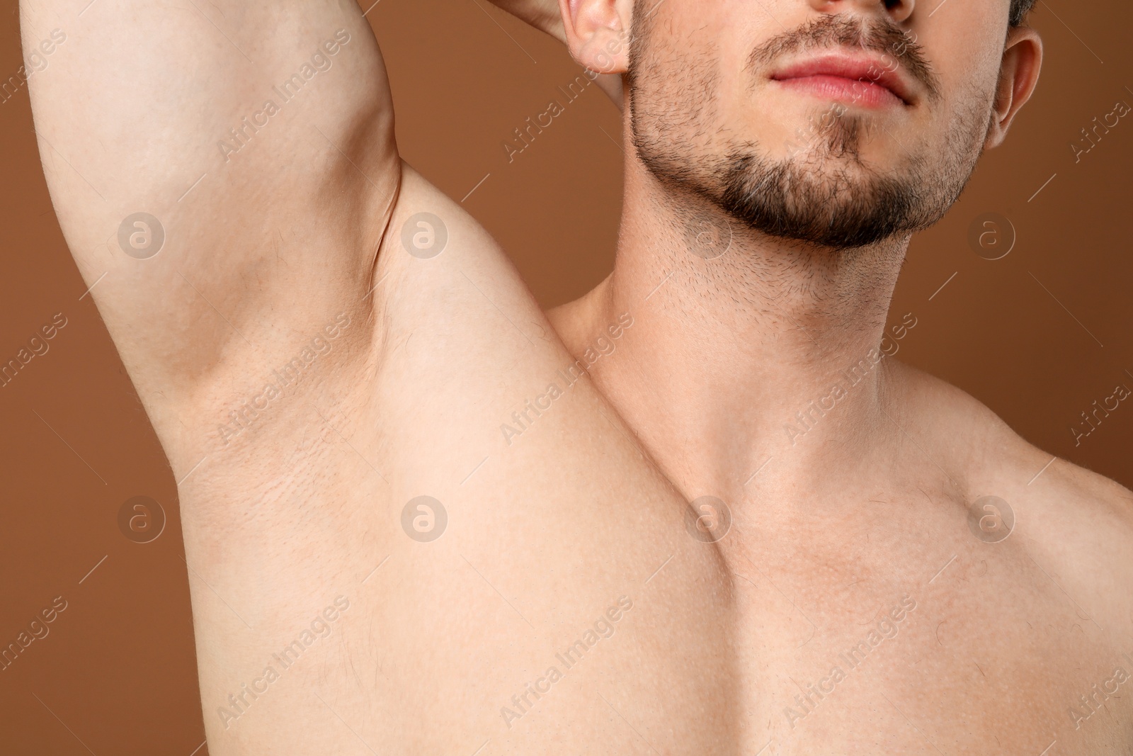 Young man showing smooth armpit after epilation procedure on brown background Photo of Young man showing smooth armpit after epilation procedure on brown background